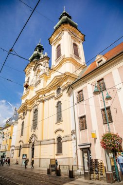 Linz, Avusturya, 27 Ağustos 2021: St. Michael Barok Ursuline Kilisesi, iki kuleli, Dar resimli cadde, güneşli yaz gününde ortaçağ şehrinin tarihi merkezinde renkli binalar.