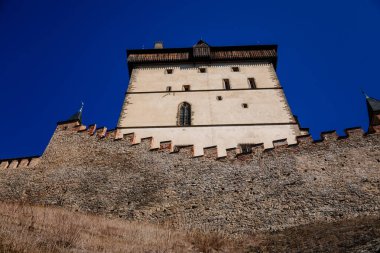 Karlstejn, Bohemya, Çek Cumhuriyeti, 12 Mart 2022: Kral 4. Charles tarafından kurulan eski bir ortaçağ Gotik kalesi, güneşli bahar gününde mavi gökyüzü, ünlü bir dönüm noktası, güçlendirilmiş surlar.