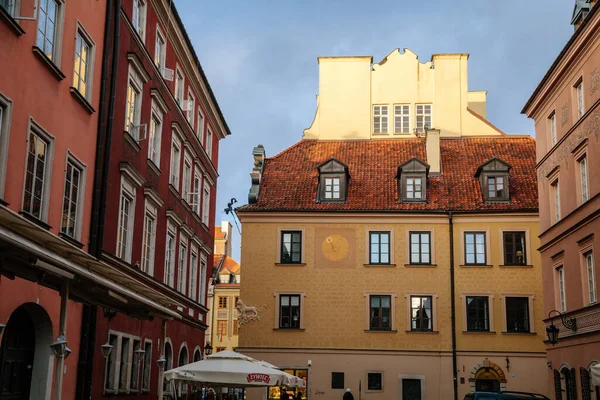 Varşova, Polonya, 13 Ekim 2021: Ortaçağ şehrinin tarihi merkezinde renkli binaları olan pitoresk cadde, Rönesans ve barok tarihi binalar. Duvarında eski güneş saati olan, güneşli bir gün.