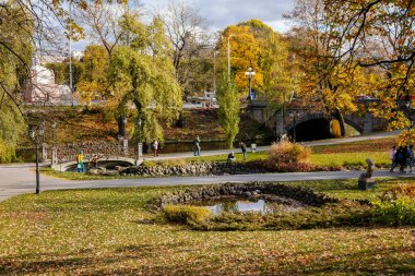 Riga, Letonya, 19 Ekim 2021: Güneşli bir sonbahar gününde Letonya Ulusal Operası yakınlarındaki güzel Bastejkalna Central Park, su üzerinde köprü