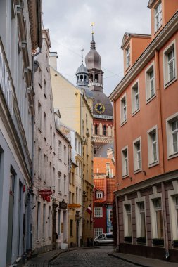 Riga, Letonya, 14 Ekim 2021: Dar resimli cadde, ortaçağ şehrinin tarihi merkezinde renkli binalar cephesi, yaz güneşli bir günde rönesans ve barok evler, ahşap pencereli kafe