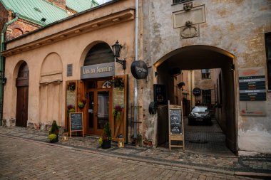 Riga, Letonya, 14 Ekim 2021: Dar resimli cadde, ortaçağ şehrinin tarihi merkezinde renkli binalar cephesi, yaz güneşli bir günde rönesans ve barok evler, ahşap pencereli kafe