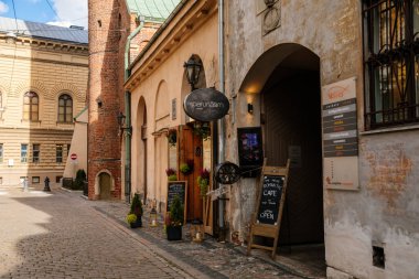 Riga, Letonya, 14 Ekim 2021: Dar resimli cadde, ortaçağ şehrinin tarihi merkezinde renkli binalar cephesi, yaz güneşli bir günde rönesans ve barok evler, ahşap pencereli kafe