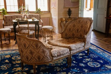 Litomysl, Çek Cumhuriyeti, 17 Nisan 2022: Barok ahşap mobilya, antika kanepe ve pencerenin yanında yumuşak koltuklar, masa başında porselen çay seti bulunan şato, oturma veya yemek odası