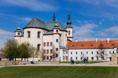 Litomysl, Çek Cumhuriyeti, 17 Nisan 2022: Kutsal Haç 'ı Bulma Kilisesi ve kalenin yakınındaki Piarist yatakhanesi, güneşli yaz gününde kulesi olan barok bina, Manastır Bahçesi Çeşmesi