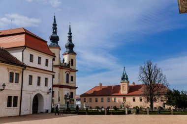 Litomysl, Çek Cumhuriyeti, 17 Nisan 2022: Şato yakınlarındaki Kutsal Haç ve Piarist Yatakhanesi Kilisesi, Güneşli yaz gününde kulesi olan Bölgesel Müze Barok Binası, taş heykeller 
