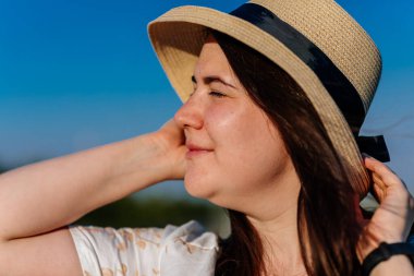 Beyaz ve bej elbiseli güzel bir kızın gün batımında haşhaş tarlasında saman şapkalı güzel bir kızın resmi, çiçekli romantik genç bir kadının portresi, pozitiflik, seçici doğal ışık.