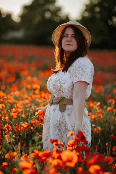 Beyaz ve bej elbiseli güzel bir kızın gün batımında haşhaş tarlasında saman şapkalı güzel bir kızın resmi, çiçekli romantik genç bir kadının portresi, pozitiflik, seçici doğal ışık.