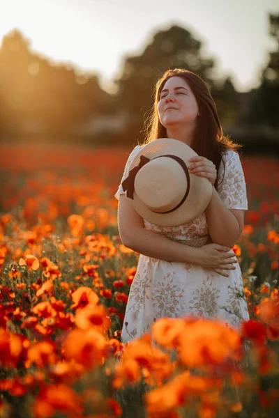 Beyaz ve bej elbiseli güzel bir kızın gün batımında haşhaş tarlasında saman şapkalı güzel bir kızın resmi, çiçekli romantik genç bir kadının portresi, pozitiflik, seçici doğal ışık.