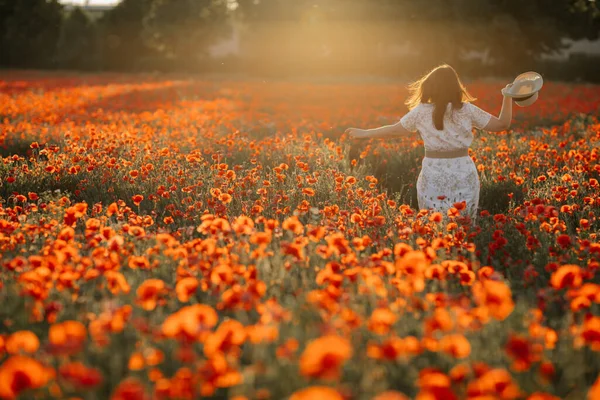 Beyaz ve bej elbiseli güzel bir kızın gün batımında haşhaş tarlasında saman şapkalı güzel bir kızın resmi, çiçekli romantik genç bir kadının portresi, pozitiflik, seçici doğal ışık.