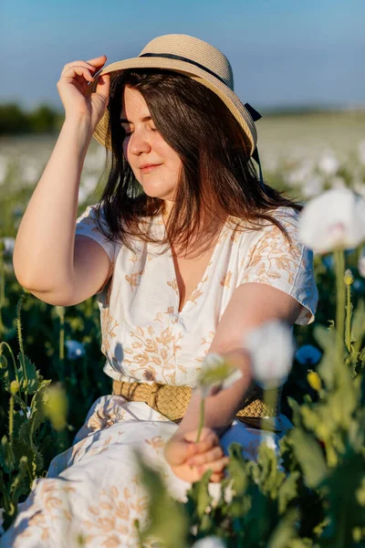 Beyaz ve bej elbiseli güzel bir kızın gün batımında haşhaş tarlasında saman şapkalı güzel bir kızın resmi, çiçekli romantik genç bir kadının portresi, pozitiflik, seçici doğal ışık.