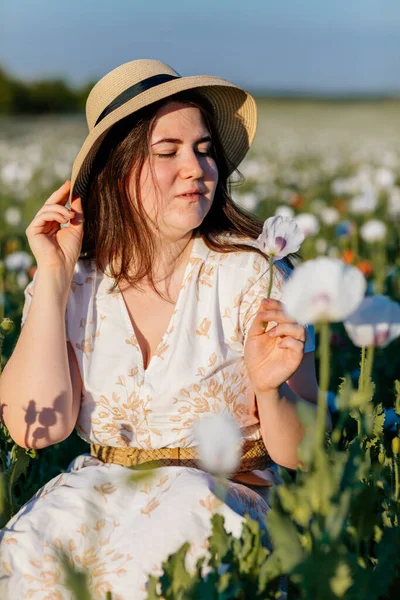 Beyaz ve bej elbiseli güzel bir kızın gün batımında haşhaş tarlasında saman şapkalı güzel bir kızın resmi, çiçekli romantik genç bir kadının portresi, pozitiflik, seçici doğal ışık.