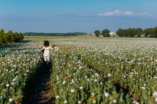 Beyaz ve bej elbiseli güzel bir kızın gün batımında haşhaş tarlasında saman şapkalı güzel bir kızın resmi, çiçekli romantik genç bir kadının portresi, pozitiflik, seçici doğal ışık.