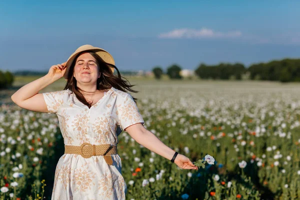Beyaz ve bej elbiseli güzel bir kızın gün batımında haşhaş tarlasında saman şapkalı güzel bir kızın resmi, çiçekli romantik genç bir kadının portresi, pozitiflik, seçici doğal ışık.