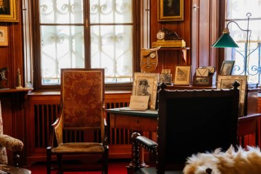 Slatinany, Czech Republic, 17 April 2022:  Castle chateau representative interior with baroque wooden carved furniture, men's office with wood paneling on walls, dishes and bottles, desk by window