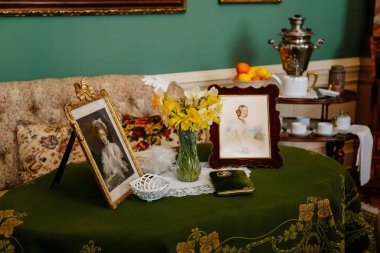 Slatinany, Czech Republic, 17 April 2022:  Castle chateau representative interior with baroque wooden carved furniture, table with green velvet tablecloth, framed portraits, yellow flowers daffodils