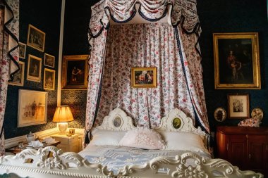 Slatinany, Czech Republic, 17 April 2022: castle chateau representative interior with baroque classic furniture, bedroom with canopy carved wooden bed, paintings and prints on wall, floral pattern