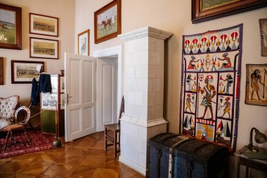 Slatinany, Czech Republic, 17 April 2022:  Castle chateau representative interior with baroque wooden carved furniture, Antique white ceramic tiled stove, paintings and photographs, Egyptian patterns 
