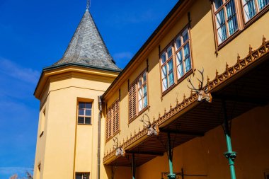 Slatinany, Czech Republic, 17 April 2022: classical chateau or romantic yellow castle surrounded by a garden, ancient aristocratic residence with park in summer sunny day, horse sculpture