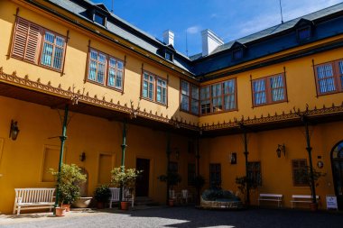 Slatinany, Czech Republic, 17 April 2022: classical chateau or romantic yellow castle surrounded by a garden, ancient aristocratic residence with park in sunny day, fountain with hunter in courtyard