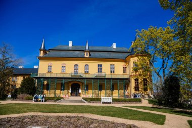 Slatinany, Czech Republic, 17 April 2022: classical chateau or romantic yellow castle surrounded by a garden, ancient aristocratic residence with park in summer sunny day