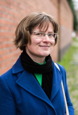 Gülümseyen 30 yaşındaki beyaz kadın tuğla bir duvara poz veriyor.