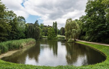 Anderlecht 'te yeşil çayırlar, ağaçlar ve su birikintisi olan bir şehir parkına bakın.