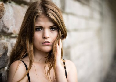 Güzel beyaz bir kadının yakın plan portresi, engebeli bir duvara dayanıyor.