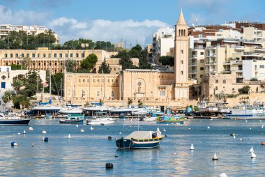Marsakala, Malta - 01 07 2022: Köy üzerinde görüş ve arka planda kilise kulesi ile liman