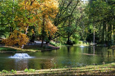 Sıcak bir sonbahar gününde Brüksel 'deki yeşil Josaphat Parkı' nın üzerinde bir çeşme ve bir gölet manzarası