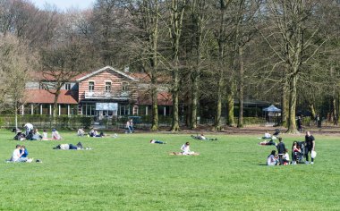 Ixelles, Brüksel / Belçika - 03: 30 2019: Güneşli bir bahar günü Bois de La Cambre şehir parkının yeşil çimlerinde yürüyen ve dinlenen karışık bir grup insan