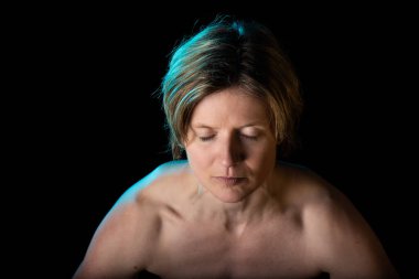 35 yaşında, çıplak omuzlu, kaslı göğsünü gösteren beyaz bir kadının stüdyo portresi.