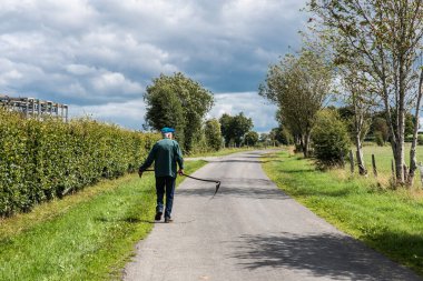 Bullingen, Walloon Regio - Doğu Belçika - 08 27 2019 Yaşlı bir çiftçi tırpan taşıyor, Azrail 'e benziyor.