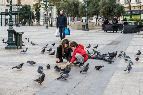 Atina Eski Kenti, Attica - Yunanistan - 12 28 2019 Kotzia Belediye Meydanı 'nda güvercinleri besleyen çocuklar