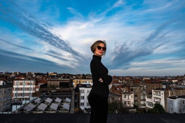 Jette, Brüksel Başkent Bölgesi - Belçika - 03 19 2020 Çekici 30 yaşında, güneş gözlüklü bir kadın çatıda poz veriyor.