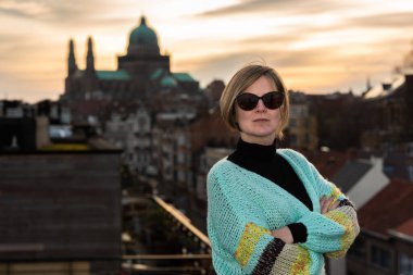 Arka planda günbatımında Brüksel silueti ile çatıda poz veren 30 yaşında çekici beyaz bir kadının portresi, Belçika