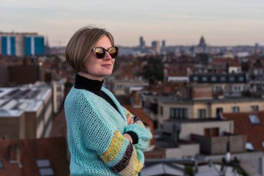 Arka planda günbatımında Brüksel silueti ile çatıda poz veren 30 yaşında çekici beyaz bir kadının portresi, Belçika