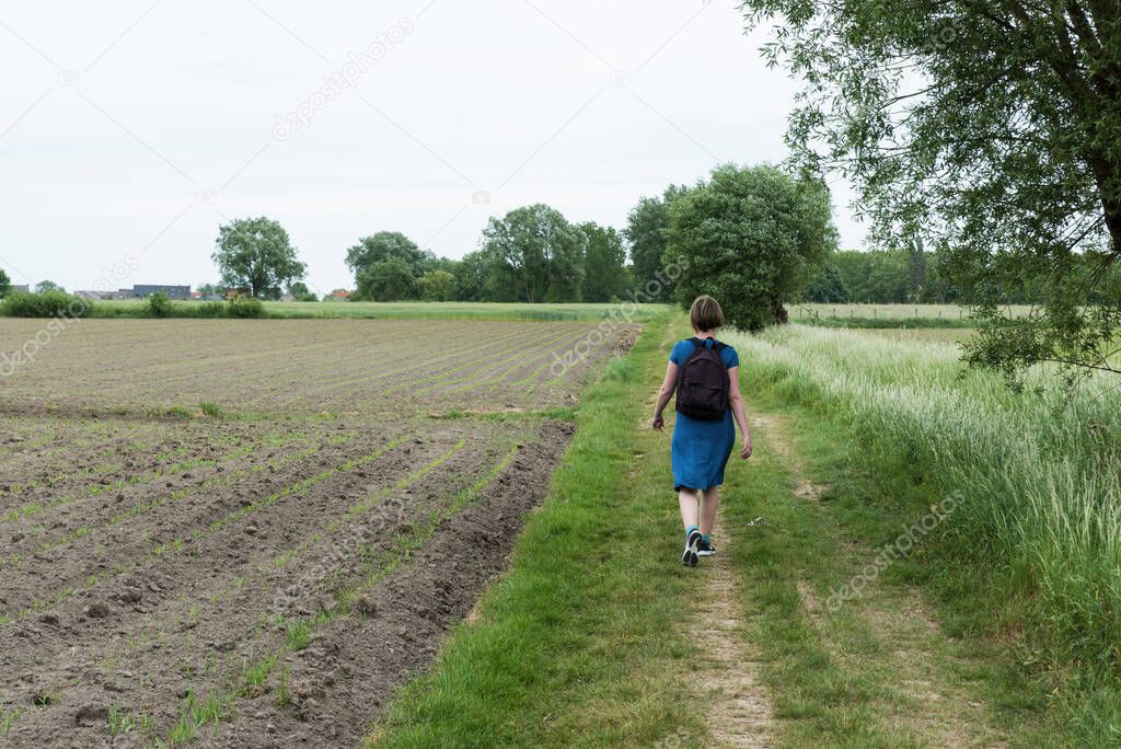 Attractive thirty year old woman in blue dress walking a trail through the Flemish countryside, Lebbeke, Belgium