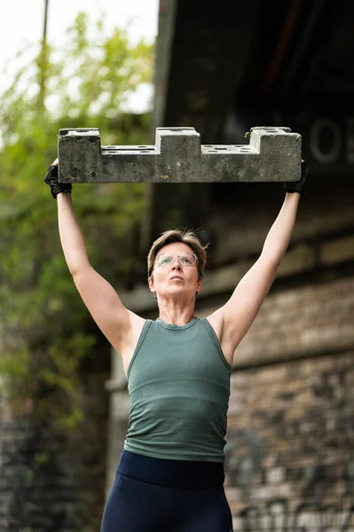 Portrait of a sporty 36 year old white woman lifting a heavy construction block, Brussels, Belgium