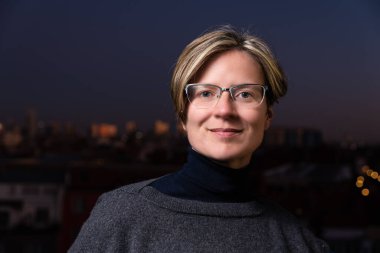 Arkaplanda günbatımında Brüksel silueti ile çatıda poz veren 30 yaşında çekici beyaz bir kadının portresi.