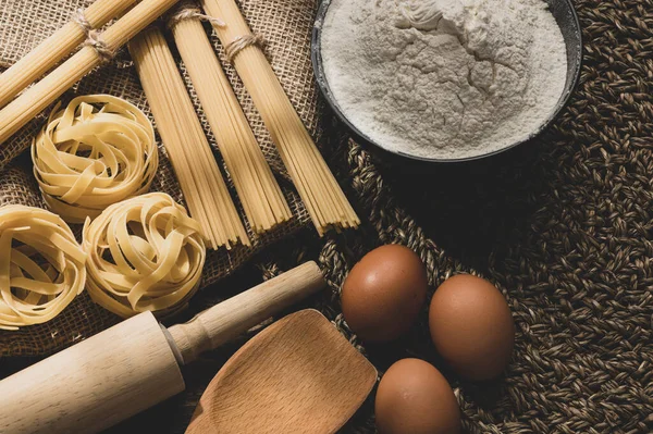 Ingredients for making pasta on a wooden background. Copy space. Uncooked pasta with flour on the table.