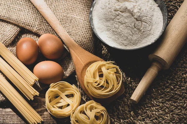 Ingredients for making pasta on a wooden background. Copy space. Uncooked pasta with flour on the table.