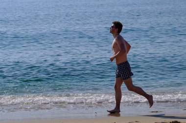 25-30 yaşlarında, esmer, esmer, güneş gözlüklü, kumlu deniz kıyısında çıplak güneş gözlüğü takan yakışıklı bir adam.