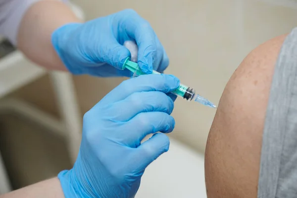 Een verpleegkundige injecteert het Covid-19 coronavirus vaccin in een oudere patiënt met een injectiespuit intramusculair in de schouder. — Stockfoto