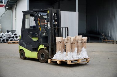 Bir yükleyici, deponun yakınındaki tesisin bahçesindeki bir konteynır gemisine boru taşır.