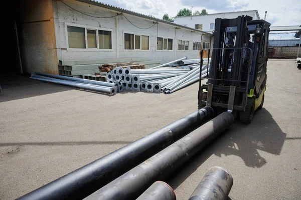Um carregador transporta tubos para um navio contêiner no quintal da fábrica perto do armazém — Fotografia de Stock