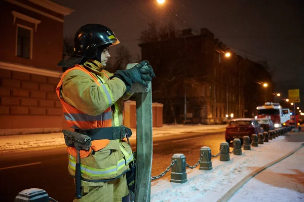 A firefighter twists a fire hose on a night street during a firefighting exercise — Stock Photo, Image