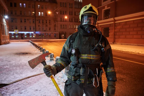Firefighters in special outfit with an ax in their hands posing on a night street — Stock Photo, Image