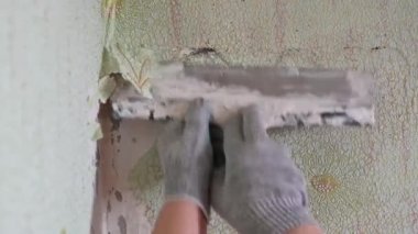 Duvardan eski duvar kağıtlarını spatula ve doğaçlama araçlarla kazımak, kendi başına bir apartman dairesini onarmak.