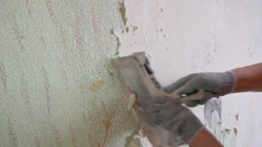 Duvardan eski duvar kağıtlarını spatula ve doğaçlama araçlarla kazımak, kendi başına bir apartman dairesini onarmak.